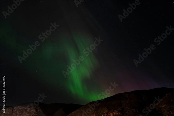 Fototapeta The Northern Lights casting an enchanting glow over the dark mountain silhouette, creating a mesmerizing contrast that draws viewers into a dreamlike, celestial experience.