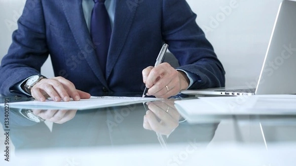 Fototapeta Businessman writing signature on contract with laptop and documents on glass desk in office. Business people concept