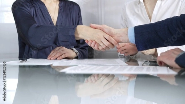 Fototapeta Unrecognizable business partners shaking hands after signing contract at glass table in office meeting, making a deal and closing agreement, close up of handshake