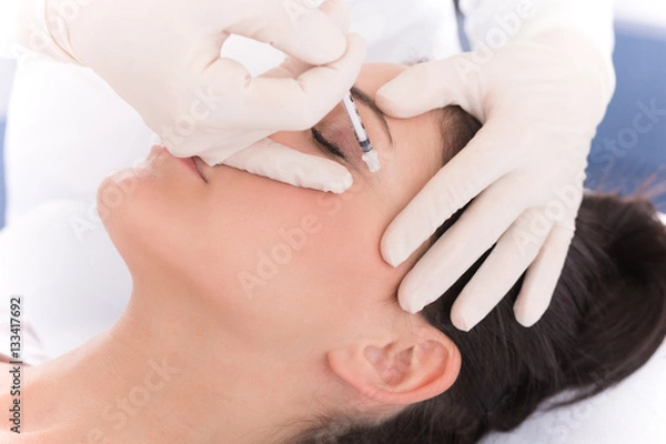 Fototapeta Cosmetologist injecting syringe in woman's face