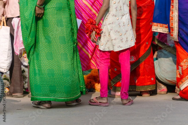Fototapeta A vibrant scene in Varanasi, India, featuring women in colorful sarees and a girl holding flowers, possibly for prayers.