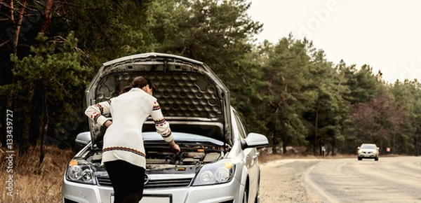 Fototapeta young woman standing near the broken car. The girl opened the hood and look at the engine. Refit woman car