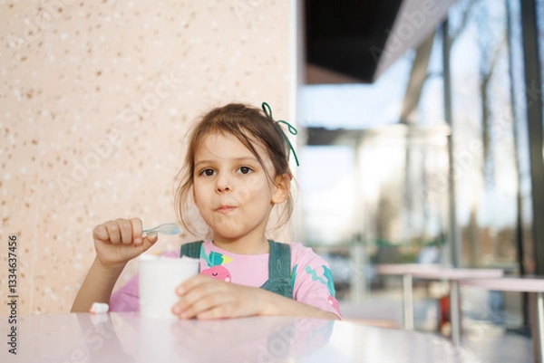 Obraz girl child eats ice cream in cafe and has fun