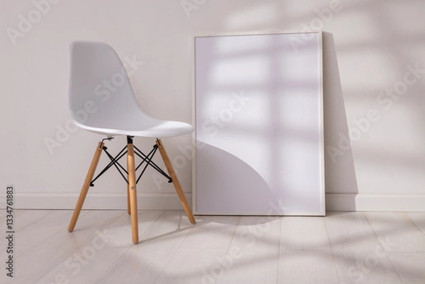 Fototapeta Mockup of empty frame in modern minimalist interior with chair and morning light on white wall background. Template for artwork, painting, photo or poster