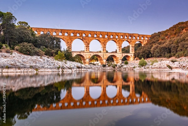 Obraz Pont du Gard, ancient Roman aqueduct bridge, Provence sunset light on arches mirroring in river, Gorges du Gardon, natural landscape designated Biosphere Reserve by UNESCO, France