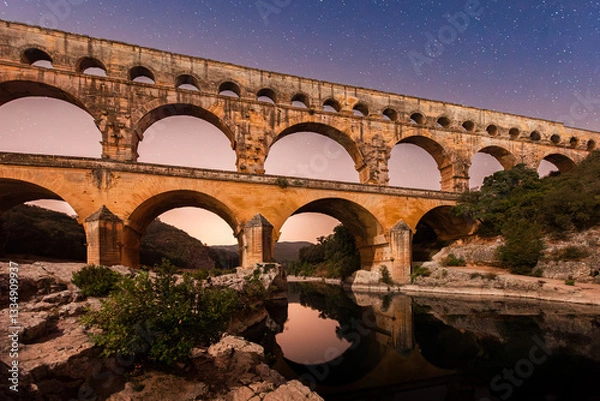 Obraz Pont du Gard, ancient Roman aqueduct bridge, colorful distant sunrise, under Provence starry night sky, Gorges du Gardon, natural landscape designated Biosphere Reserve by UNESCO, France