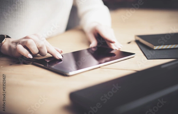 Fototapeta Closeup view of female finger touching black screen digital tablet under the wooden table.Concept young business people using mobile devices.Horizontal, blurred background.