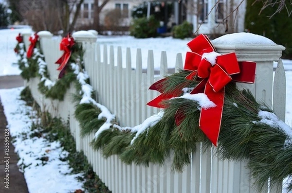 Obraz Snow covered evergreen garland draped along a white picket fence