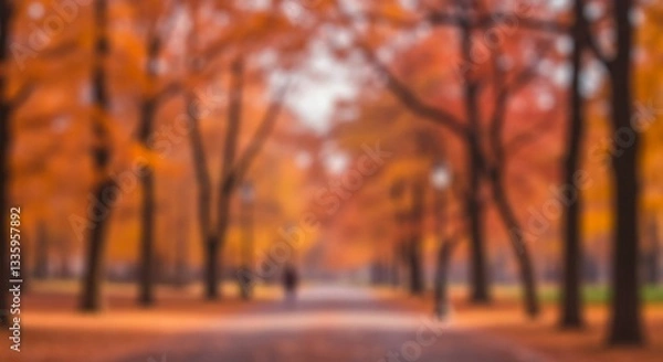Fototapeta A warm, dreamy atmosphere with vertical tree trunks is created by a blurred autumn forest scene with golden-orange foliage and sunlight bokeh effect