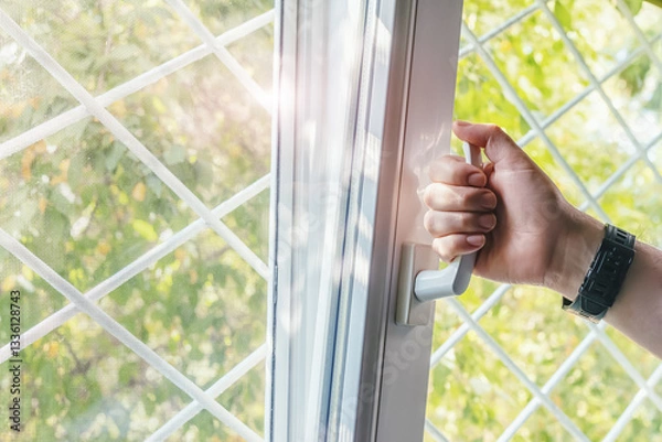 Obraz Male hand opens a plastic window with a metal grate, letting in fresh air and sunlight. Manual opening white plastic pvc window at home.