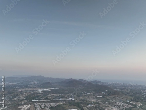 Fototapeta Aerial panoramic view of a vast rural landscape with distant mountain ranges under a clear blue sky, featuring a diagonal airplane contrail stretching across the horizon