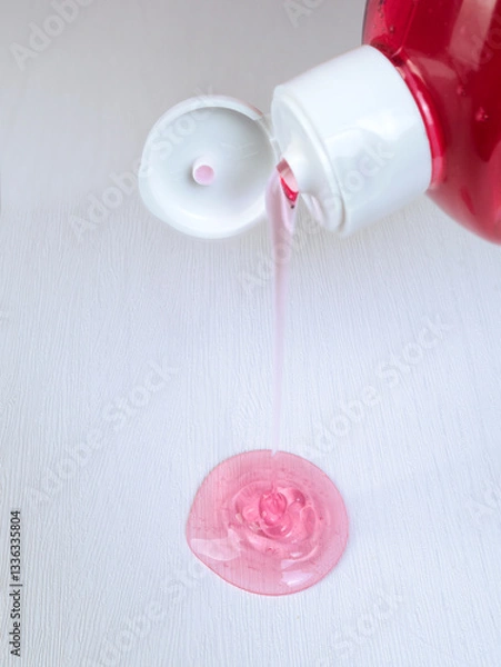 Fototapeta A stream of pink shower gel from a bottle flows onto a white table