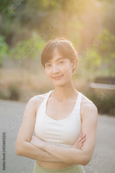 Fototapeta Asian woman outdoor workout. Healthy and active lifestyle concept. She smiles confidently in serene park setting with sunlight filtering through