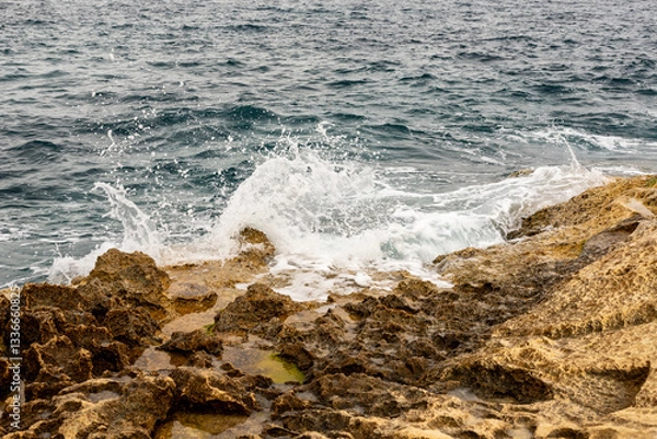 Obraz Dramatic Adriatic Sea waves crash against the rugged limestone coast. Powerful waves hit the yellow rocks of Malta’s seashore on a sunny spring day, creating a breathtaking coastal scene.