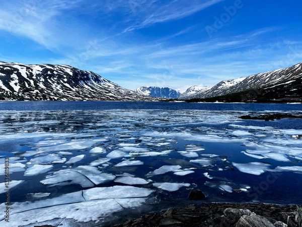 Fototapeta Scenic view of a frozen lake with ice floes in the foreground and a black, snow-covered mountain range in the background