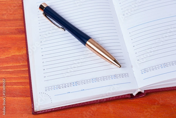 Fototapeta Business accessories - diary with a pen lying on a wooden table