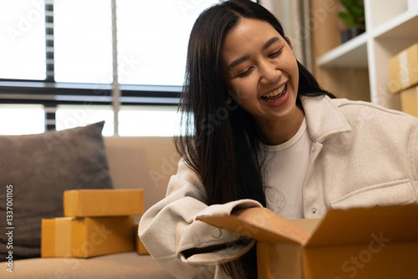 Fototapeta A woman is holding two boxes and smiling. She is sitting in front of a laptop. The boxes are brown and appear to be gifts. The woman seems happy and excited about the boxes
