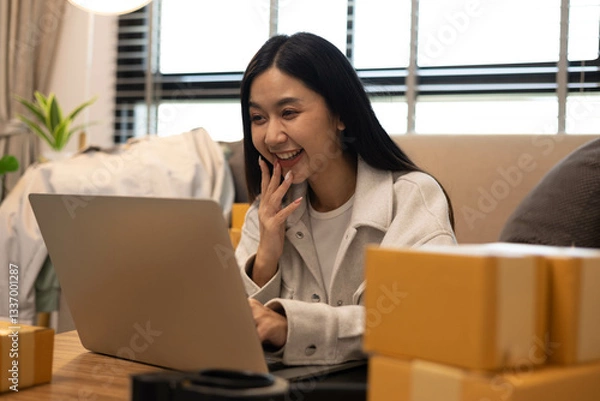 Fototapeta A woman is holding two boxes and smiling. She is sitting in front of a laptop. The boxes are brown and appear to be gifts. The woman seems happy and excited about the boxes
