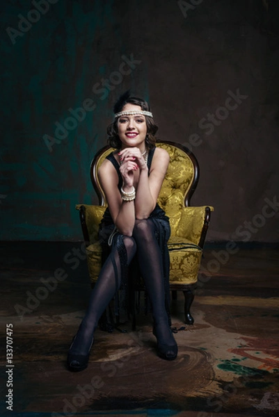 Fototapeta Young beautiful girl in red dress style of the 20's or 30's with glass of martini near the piano. Vintage style beautiful woman. Old fashioned makeup and retro finger wave hairstyle.