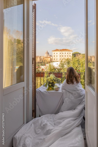Fototapeta A woman wrapped in a soft white blanket enjoys a peaceful morning on a charming balcony in Rome, overlooking St Peters Basilica