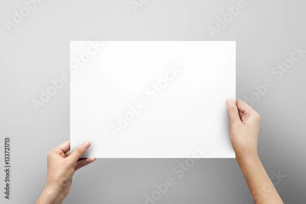 Fototapeta Woman hand holding blank paper sheet A4 size or letter paper on grey background.
