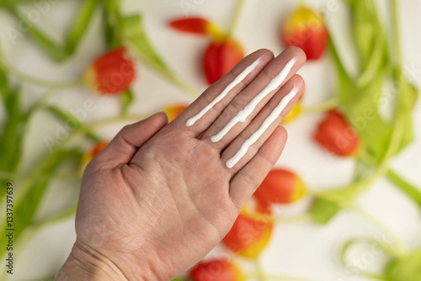 Fototapeta A person applying the correct amount of sunscreen for the face and neck – three finger lengths, with tulips in the background. Concept of applying sunscreen in spring. 