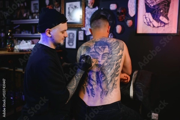 Obraz Tattoo artist man with black gloves draws a knight tattoo on the guy's back in the studio. Tattoo artist's workflow