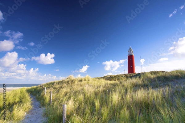 Fototapeta a red lighthousein the dunes with a blue sky in summer