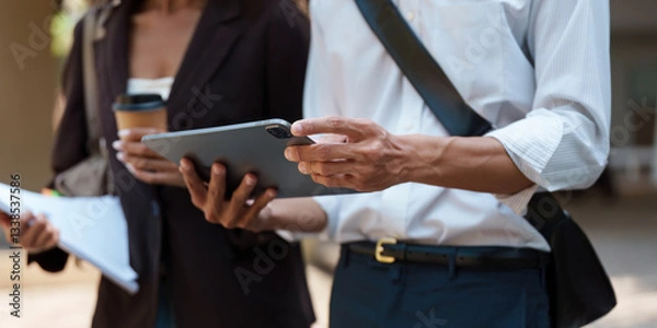 Fototapeta Sustainability and Technology. Two professionals discussing sustainable practices using a tablet in an outdoor setting.
