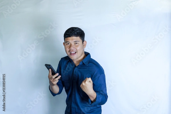 Obraz feeling happy excited modern successful young man holding the phone and raising his hand 