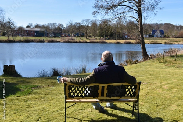 Fototapeta Mann sitzt an einem See auf einer Bank