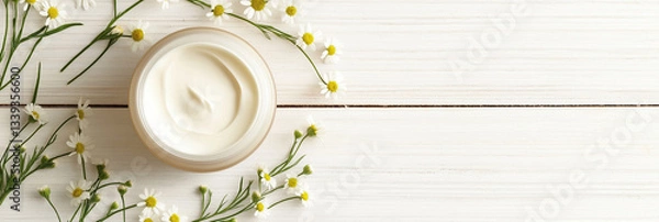 Obraz Natural skincare cream in jar surrounded by small white flowers and green leaves on wooden background
