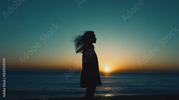 Fototapeta A silhouette of a person stands against a vibrant sunset over the ocean, creating a serene and contemplative atmosphere. 
