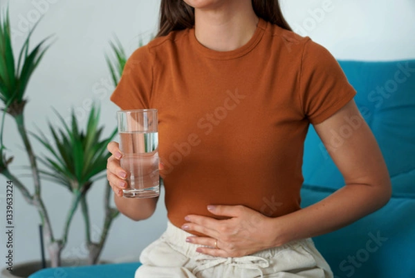 Fototapeta Eating Disorder. Unrecognizable girl suffering from abdominal pain holds a glass of water in her hand. Unregulated Intestine.