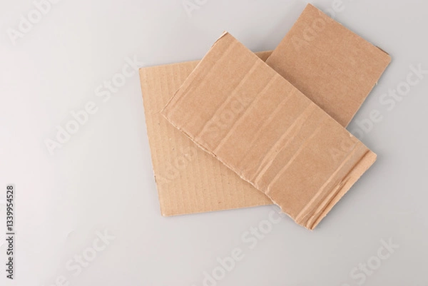 Obraz step in creative process, recycled paper materials for crafting, two pieces of cardboard placed on a grey surface. The top piece of cardboard is slightly smaller and has visible vertical ridges,