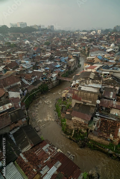 Fototapeta Vertical drone image of high densely populated residential area with dirty river at Bandung City, 2025. West Java, Indonesia.