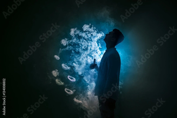 Fototapeta The man smoke an electronic cigarette with a ring against the background of the blue light