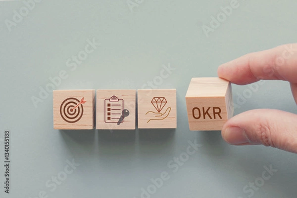 Fototapeta Hands holding wooden blocks with OKR icons, objective and key results concept
