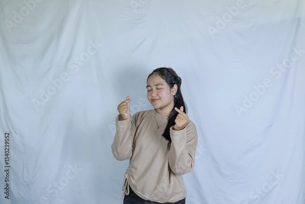 Obraz a young girl wearing a gray t-shirt with a cheerful expression and making a love symbol with her fingers. advertising theme concept studio photo