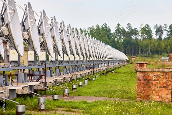Fototapeta A row of solar radio telescope dishes against a forest background
