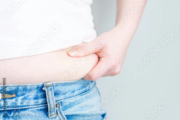 Obraz A woman's hand holds belly on gray background, concept of obesity.