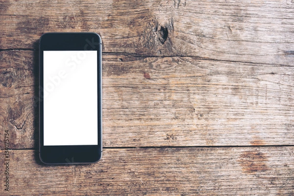 Fototapeta Mockup image of black mobile phone with blank white screen on vintage wood table background