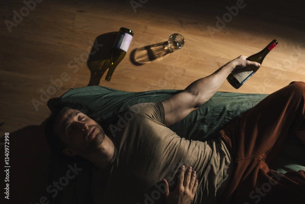 Fototapeta A man lies on a bed with empty alcohol bottles next to him