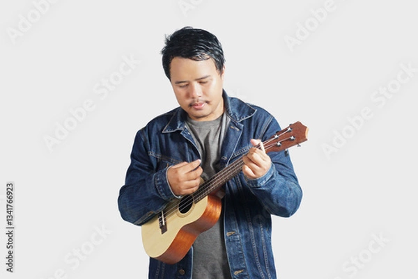 Fototapeta a southeast asian man is playing the ukulele very energetically with plain background     