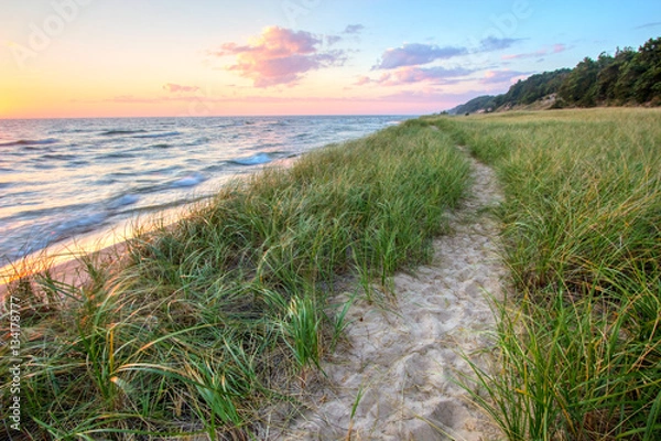 Fototapeta Spacer po plaży. Piaszczysta trasa wije się wzdłuż plaży Wielkich Jezior z horyzontem zachodzącego słońca i wydmami w tle. Muskegon w stanie Michigan.