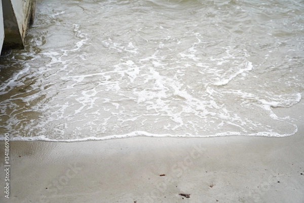 Fototapeta Gentle waves roll across a sandy beach, creating a rhythmic, calming scene as water meets shore—perfect for tranquil visuals or nature backgrounds. 