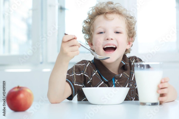 Fototapeta Boy eating cereal while having breakfast  in the kitchen.