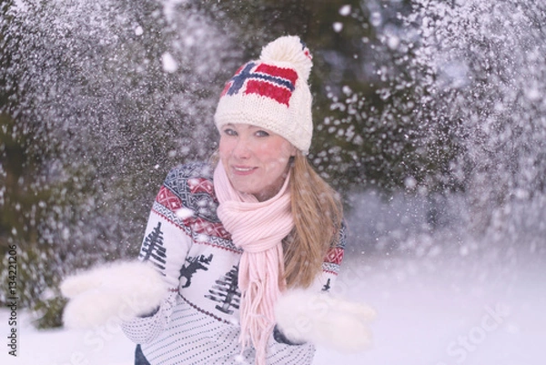 Fototapeta Woman in hat with Norway flag and scandinavian sweater has fun in winter forest. Blowing snow