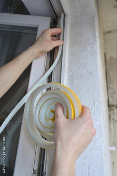 Obraz A man insulates windows and balcony doors with foam adhesive tape. Budget renovation in the apartment. Preparation for the cold snap. Heating problem in apartment buildings