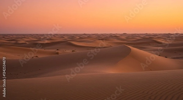 Fototapeta Endless sand dunes under a twilight sky. Warm orange and pink hues blend softly with the desert landscape, with rippled sand patterns adding texture